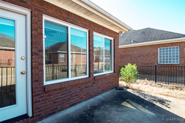 view of property exterior featuring roof with shingles, fence, and brick siding