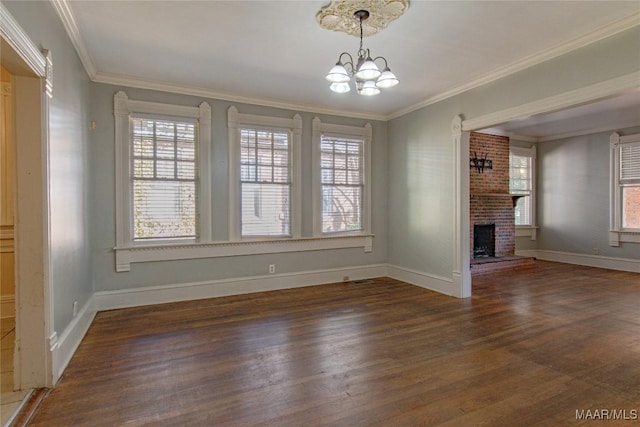 unfurnished dining area featuring a chandelier, baseboards, ornamental molding, a brick fireplace, and dark wood-style floors