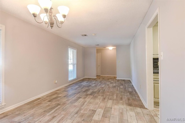 empty room with baseboards, visible vents, an inviting chandelier, a textured ceiling, and light wood-style floors