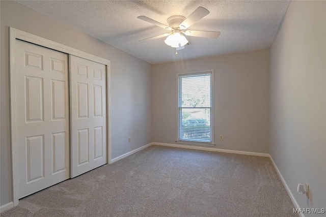 unfurnished bedroom featuring a closet, light colored carpet, a textured ceiling, and baseboards