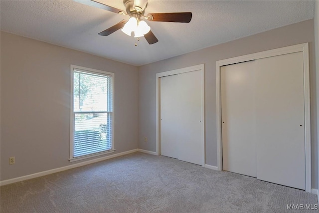 unfurnished bedroom featuring two closets, light colored carpet, a ceiling fan, a textured ceiling, and baseboards