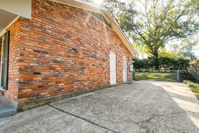 view of property exterior with driveway, brick siding, and a gate