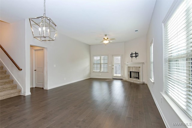 unfurnished living room featuring stairs, dark wood-type flooring, ceiling fan with notable chandelier, and a fireplace