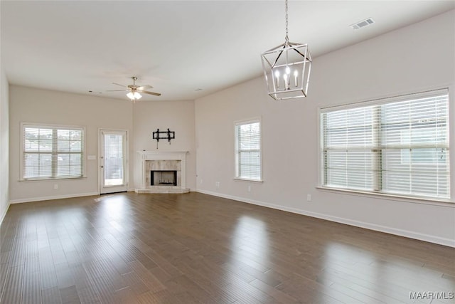 unfurnished living room featuring ceiling fan with notable chandelier, dark wood-style flooring, a fireplace, visible vents, and baseboards