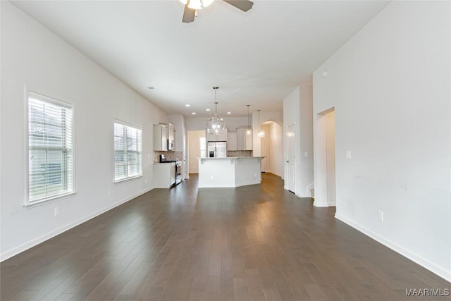 unfurnished living room featuring baseboards, arched walkways, ceiling fan, dark wood-type flooring, and recessed lighting