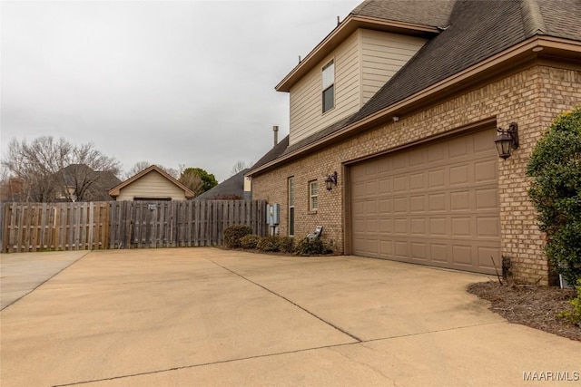 view of property exterior featuring driveway, roof with shingles, fence, and brick siding