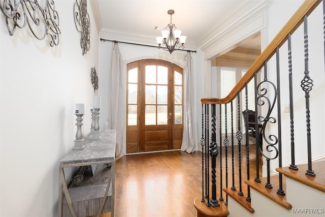 entryway with arched walkways, ornamental molding, wood finished floors, stairs, and a notable chandelier