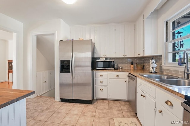 kitchen featuring light tile patterned floors, stainless steel appliances, a sink, white cabinetry, and backsplash