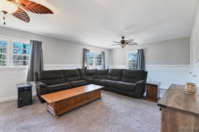 living area with a ceiling fan, a wainscoted wall, and light colored carpet