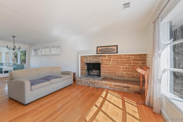 living room with light wood-type flooring, a brick fireplace, visible vents, and an inviting chandelier