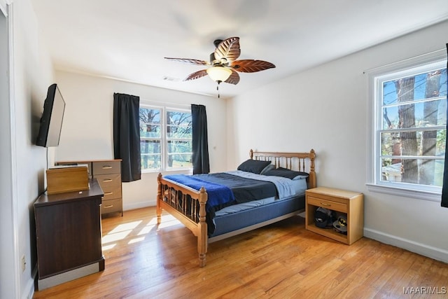 bedroom featuring baseboards, multiple windows, ceiling fan, and light wood finished floors