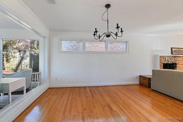 unfurnished dining area featuring a fireplace, crown molding, a notable chandelier, and wood finished floors