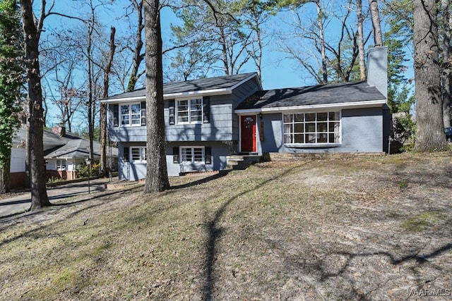 split level home with entry steps, brick siding, a chimney, and a front lawn