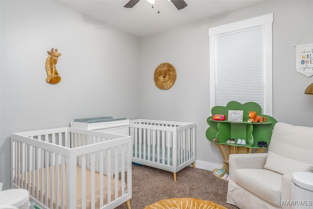 carpeted bedroom with ceiling fan, a crib, and baseboards