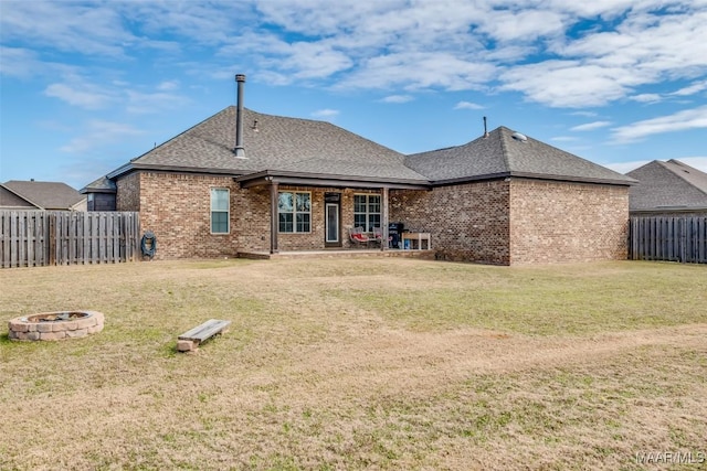 rear view of property with brick siding, a yard, a shingled roof, fence, and a fire pit