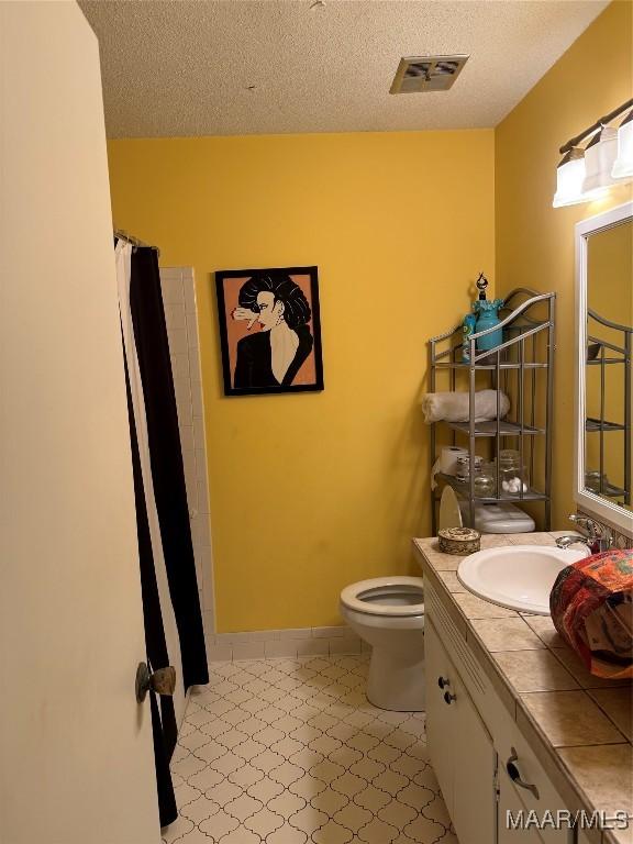 full bath featuring visible vents, toilet, vanity, and a textured ceiling