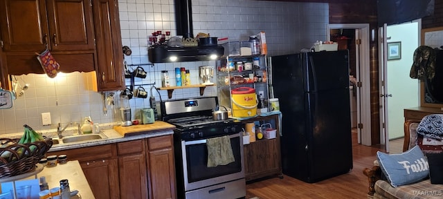 kitchen featuring wood finished floors, a sink, freestanding refrigerator, decorative backsplash, and stainless steel gas stove