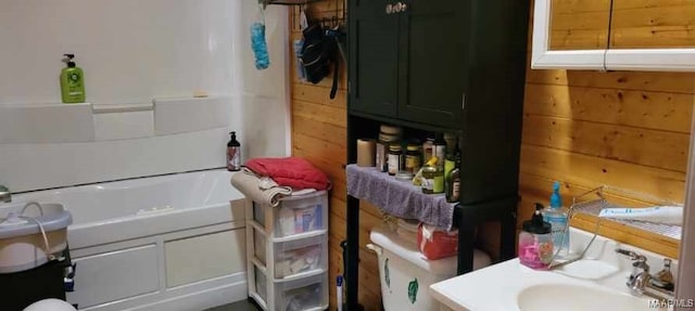 full bath featuring a tub, a sink, and wooden walls