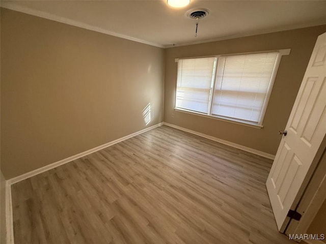 empty room featuring baseboards, light wood-style flooring, visible vents, and crown molding