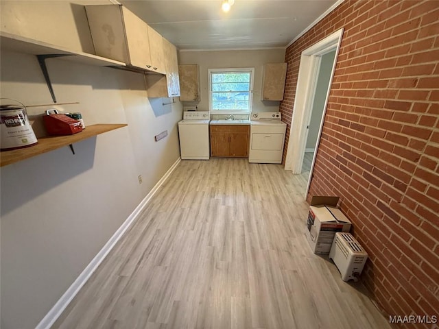 kitchen featuring washer and clothes dryer, light wood-style flooring, a sink, brick wall, and baseboards