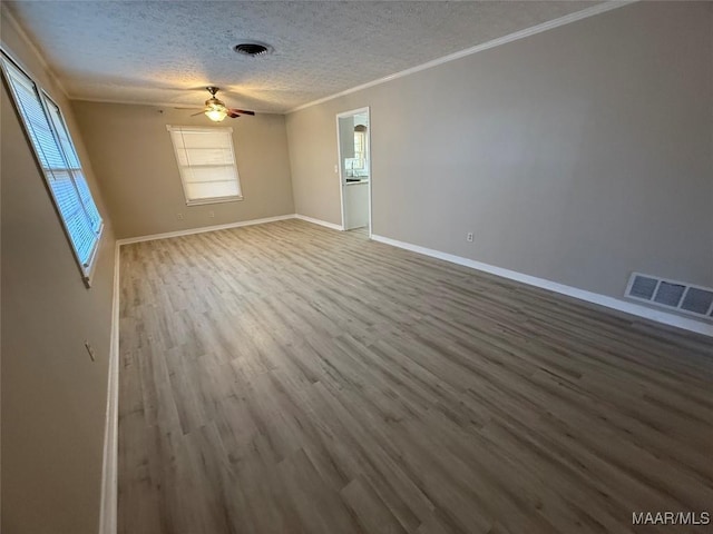 empty room featuring a textured ceiling, a wealth of natural light, wood finished floors, and visible vents