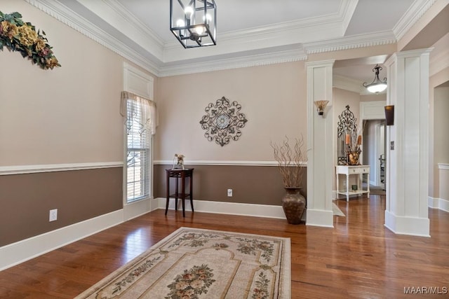 foyer entrance with dark wood-style floors, decorative columns, a tray ceiling, and crown molding