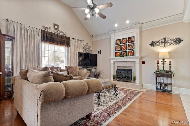 living room featuring high vaulted ceiling, a fireplace, wood finished floors, baseboards, and crown molding