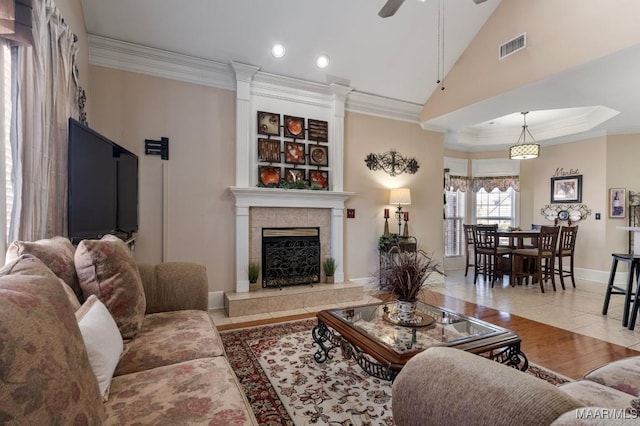 living room with light tile patterned floors, ceiling fan, a fireplace, visible vents, and crown molding