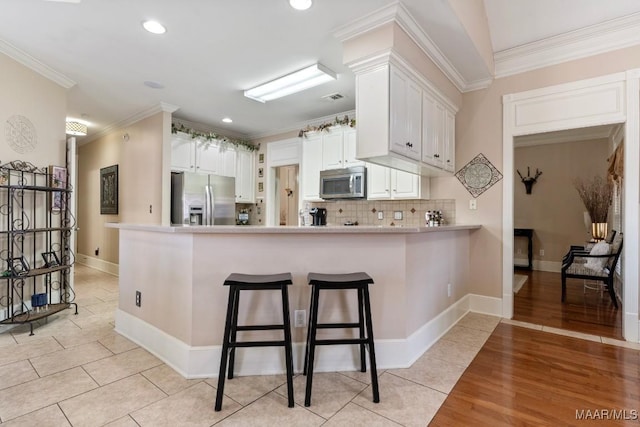 kitchen with white cabinets, ornamental molding, a peninsula, stainless steel appliances, and light countertops