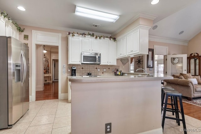 kitchen with white cabinets, appliances with stainless steel finishes, a breakfast bar, open floor plan, and light countertops