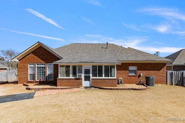 back of property with a yard, central AC, brick siding, and fence