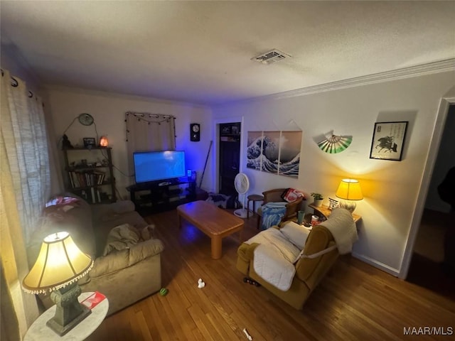 living area with ornamental molding, visible vents, baseboards, and wood finished floors