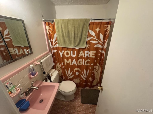 full bathroom featuring a textured ceiling, tile patterned flooring, toilet, a sink, and tile walls