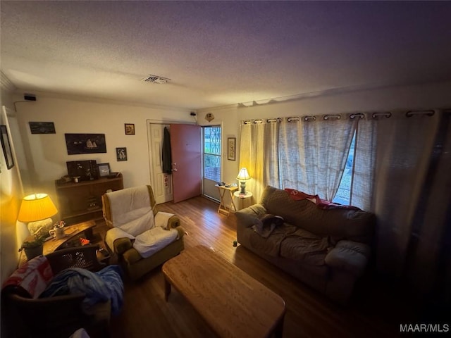 living area featuring a textured ceiling, wood finished floors, visible vents, and crown molding