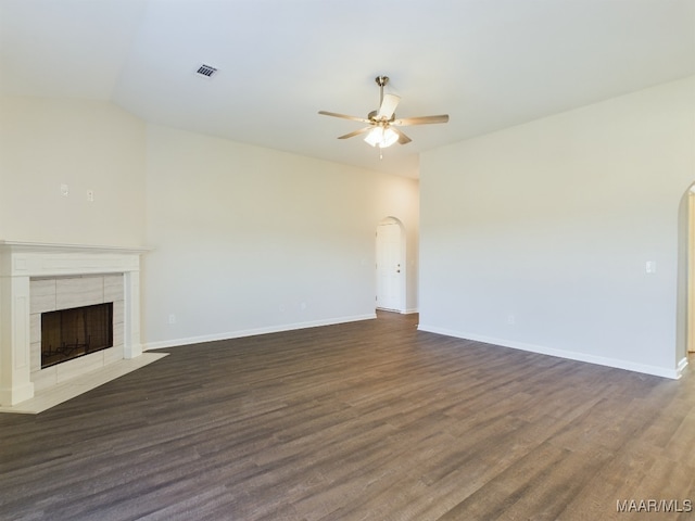 unfurnished living room featuring arched walkways, dark wood-style flooring, visible vents, a tiled fireplace, and a ceiling fan