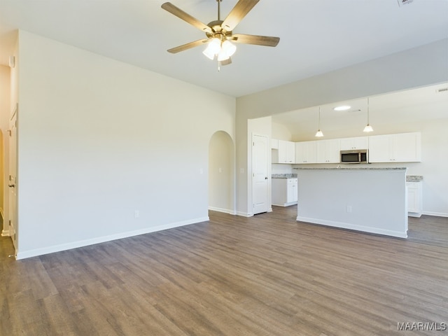 unfurnished living room with ceiling fan, arched walkways, dark wood finished floors, and baseboards