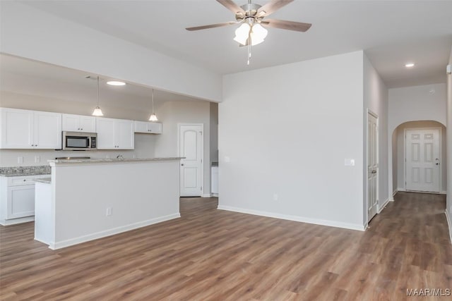 kitchen featuring arched walkways, white cabinets, stainless steel microwave, dark wood-style flooring, and hanging light fixtures