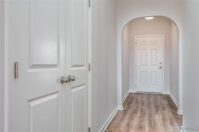 hall with arched walkways, light wood-style flooring, and baseboards