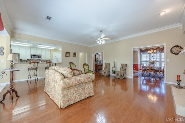 living area with visible vents, crown molding, light wood-style flooring, and baseboards