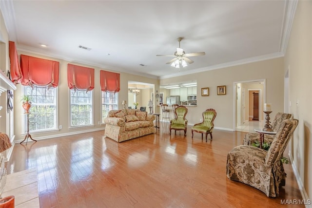 living room featuring crown molding, visible vents, wood finished floors, and ceiling fan with notable chandelier