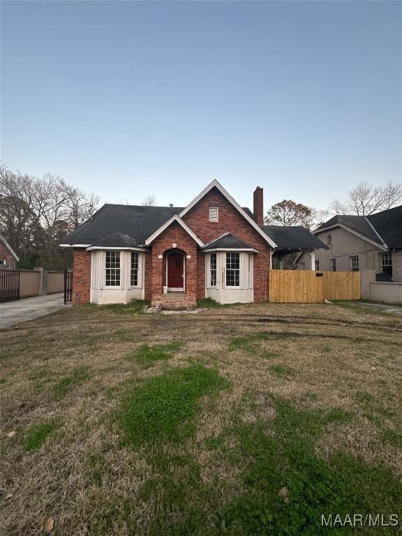 view of front of home featuring a front yard, a chimney, fence, and brick siding