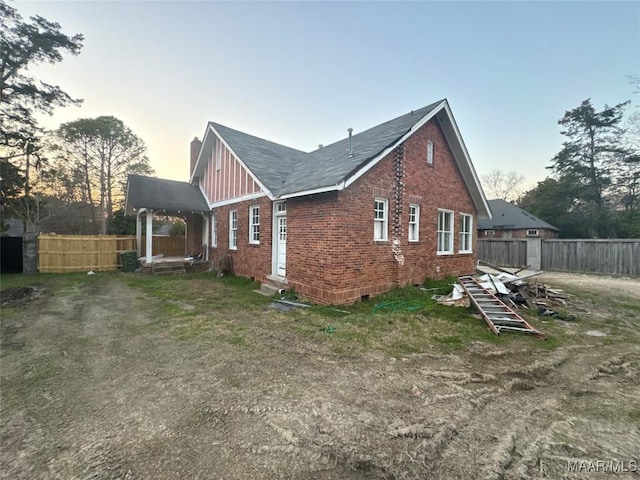 property exterior at dusk with entry steps, brick siding, fence, and a chimney