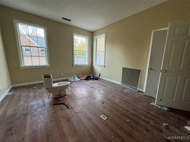 interior space featuring a textured ceiling, dark wood-style flooring, visible vents, and baseboards