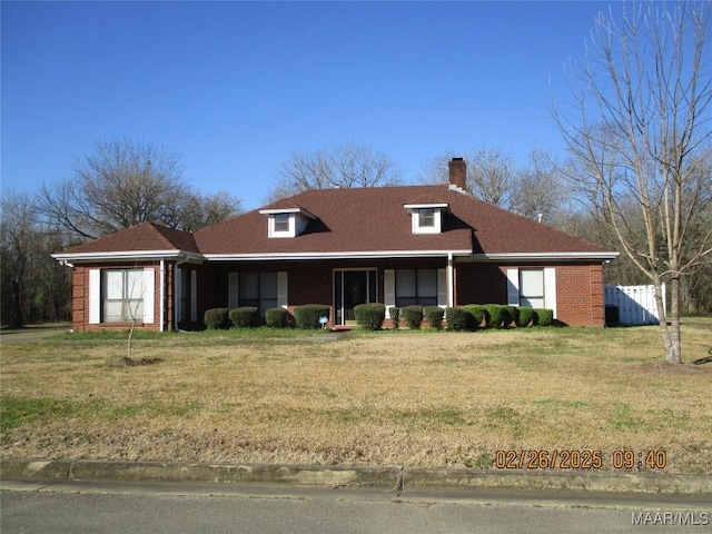 view of front of house featuring brick siding, a chimney, roof with shingles, fence, and a front yard