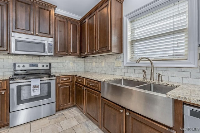 kitchen featuring backsplash, light stone counters, stainless steel appliances, and a sink