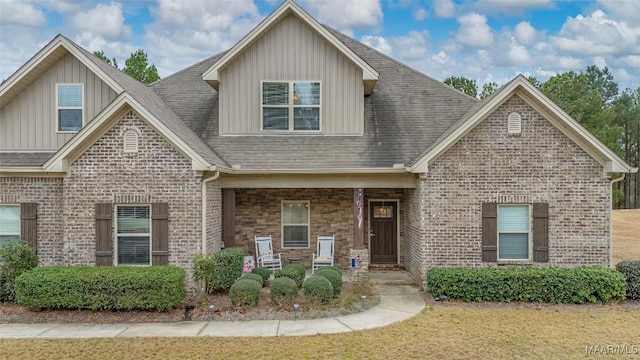 craftsman house with covered porch, a shingled roof, board and batten siding, and brick siding