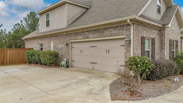 view of side of home featuring board and batten siding, brick siding, fence, and a garage