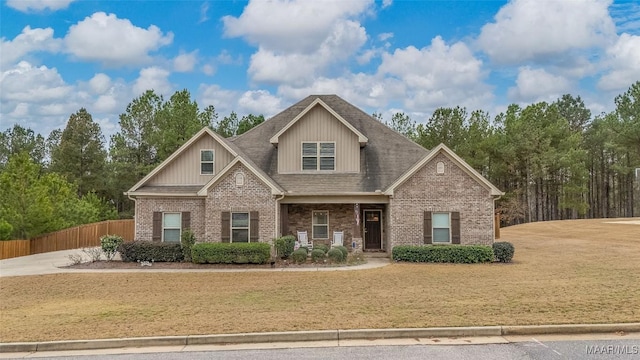 craftsman-style home featuring a shingled roof, brick siding, fence, and a front lawn