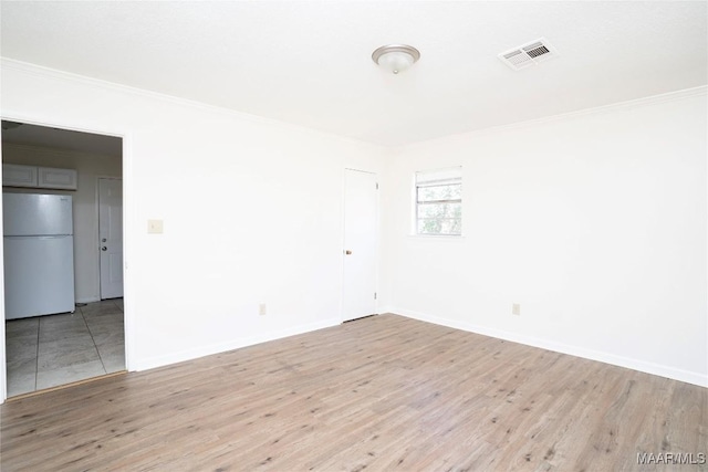 empty room with light wood-style floors, visible vents, ornamental molding, and baseboards