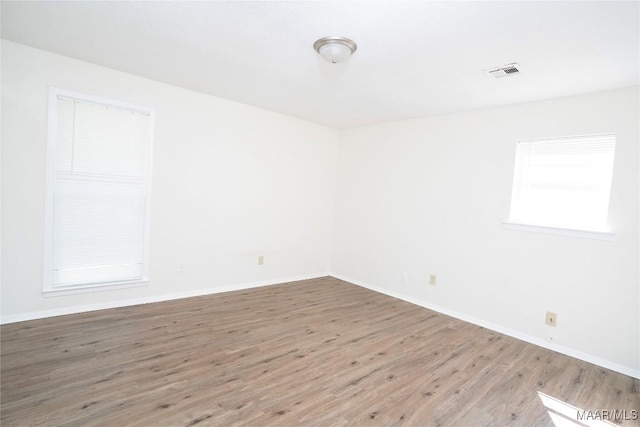 empty room with wood finished floors, visible vents, and baseboards